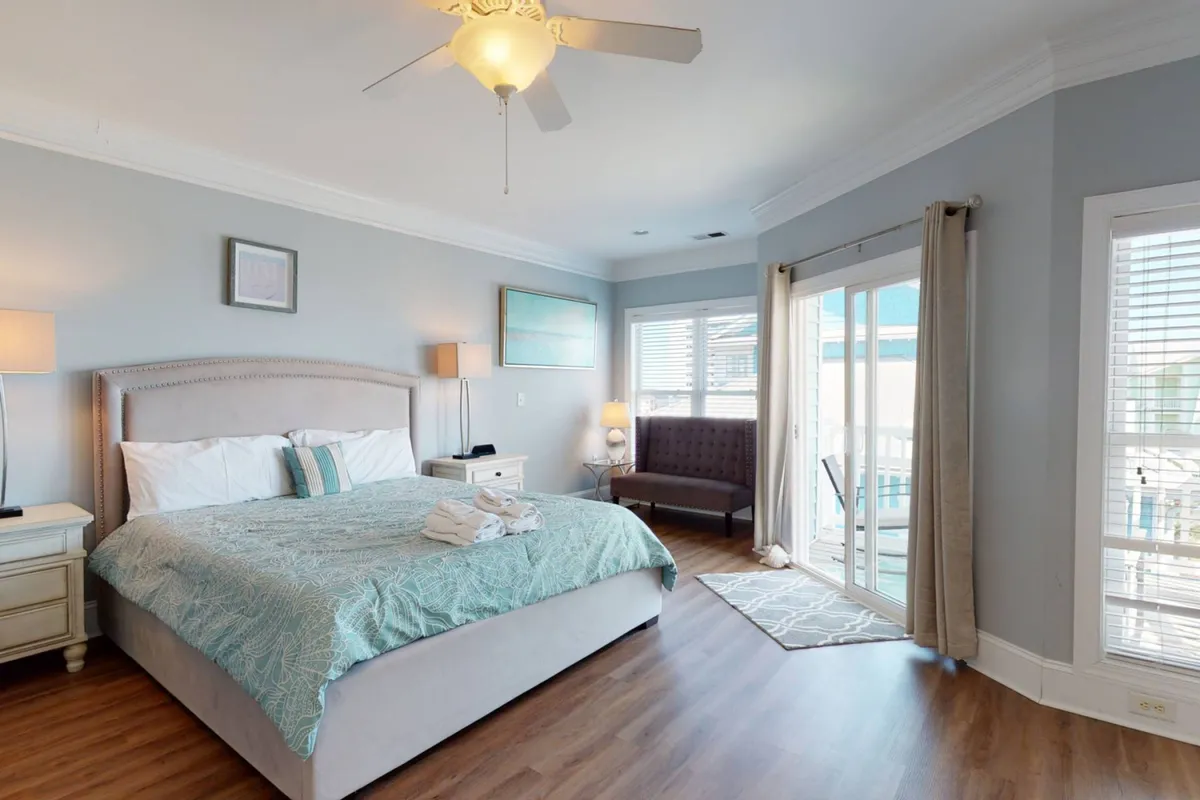 A bright and serene bedroom featuring a bed with patterned bedding, a cozy sofa positioned by the window, and a door leading out to a private balcony. Natural light fills the space, highlighting the restful atmosphere and inviting comfort.