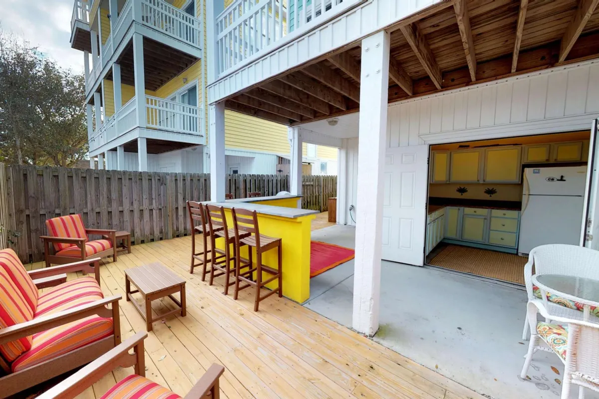 The image showcases the vibrant exterior deck area of the townhouse, featuring a colorful array of chairs around an inviting outdoor bar. The space is designed for entertaining and relaxing, perfect for sunset gatherings, barbecues, and celebrations with friends and family.