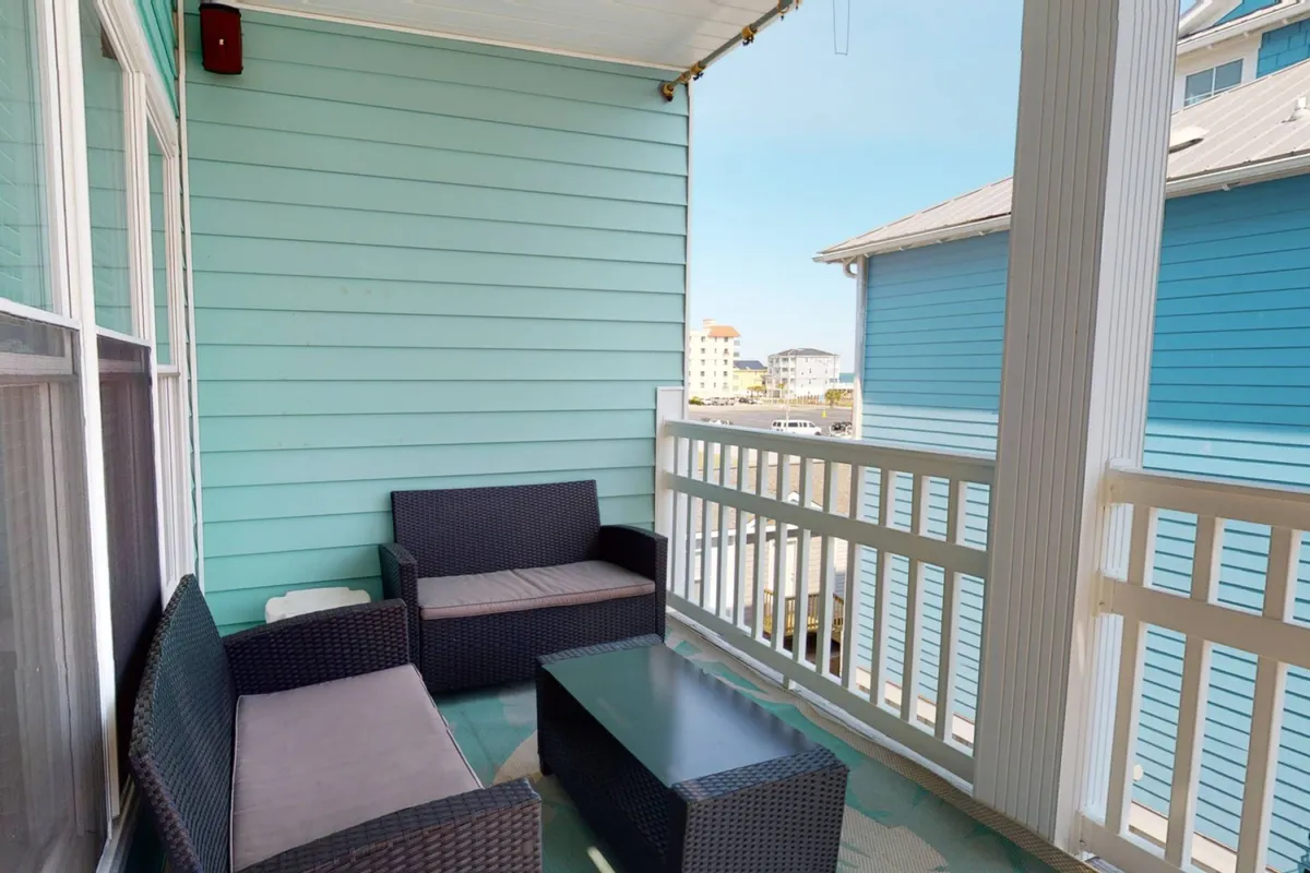 A cozy outdoor lounge setting with comfortable wicker seating, a coffee table, and a blue wall backdrop. The space is designed for outdoor enjoyment, perfect for casual drinks or evening conversations under the stars.