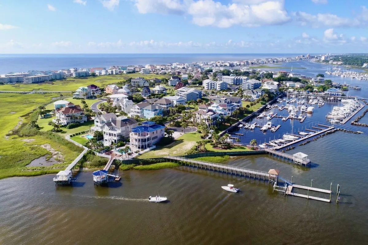 A vibrant marina scene showing boats moored at the docks, waterfront houses, and green spaces. The area is lively yet relaxed, evoking a sense of coastal community and access to water-based activities.