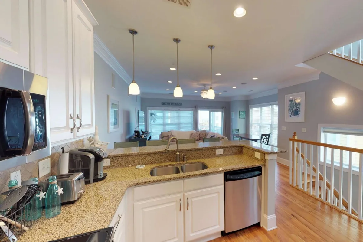 A welcoming kitchen scene featuring a granite countertop, stainless steel appliances, pendant lighting, and an open view into the living space. The image hints at culinary creativity and modern amenities, supporting activities like shared meals and casual dining.
