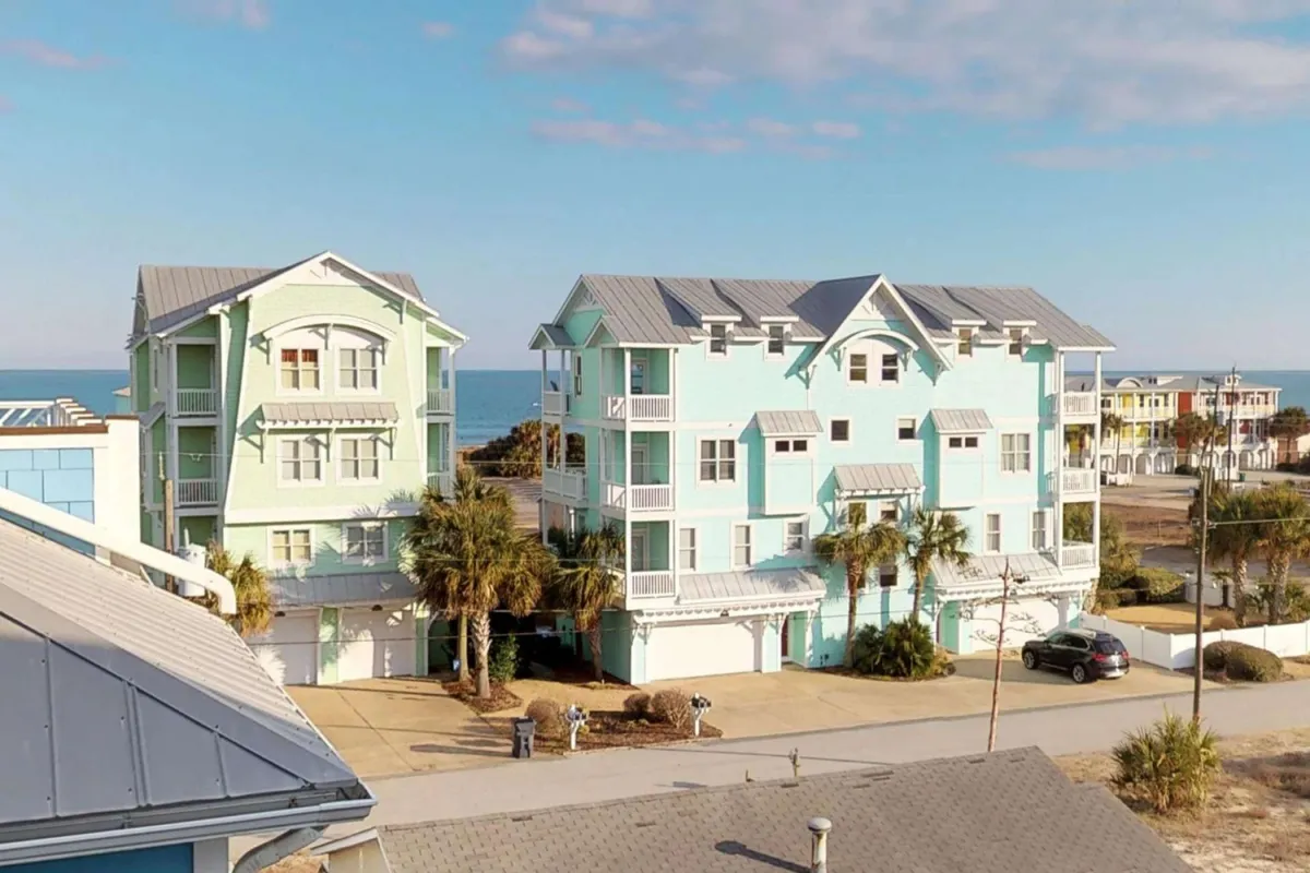 This image showcases a row of colorful coastal homes lined with palm trees and offering expansive ocean views. The bright, cheerful exterior hints at a lively, social beach atmosphere, with balconies and porches that invite outdoor gatherings and relaxation.